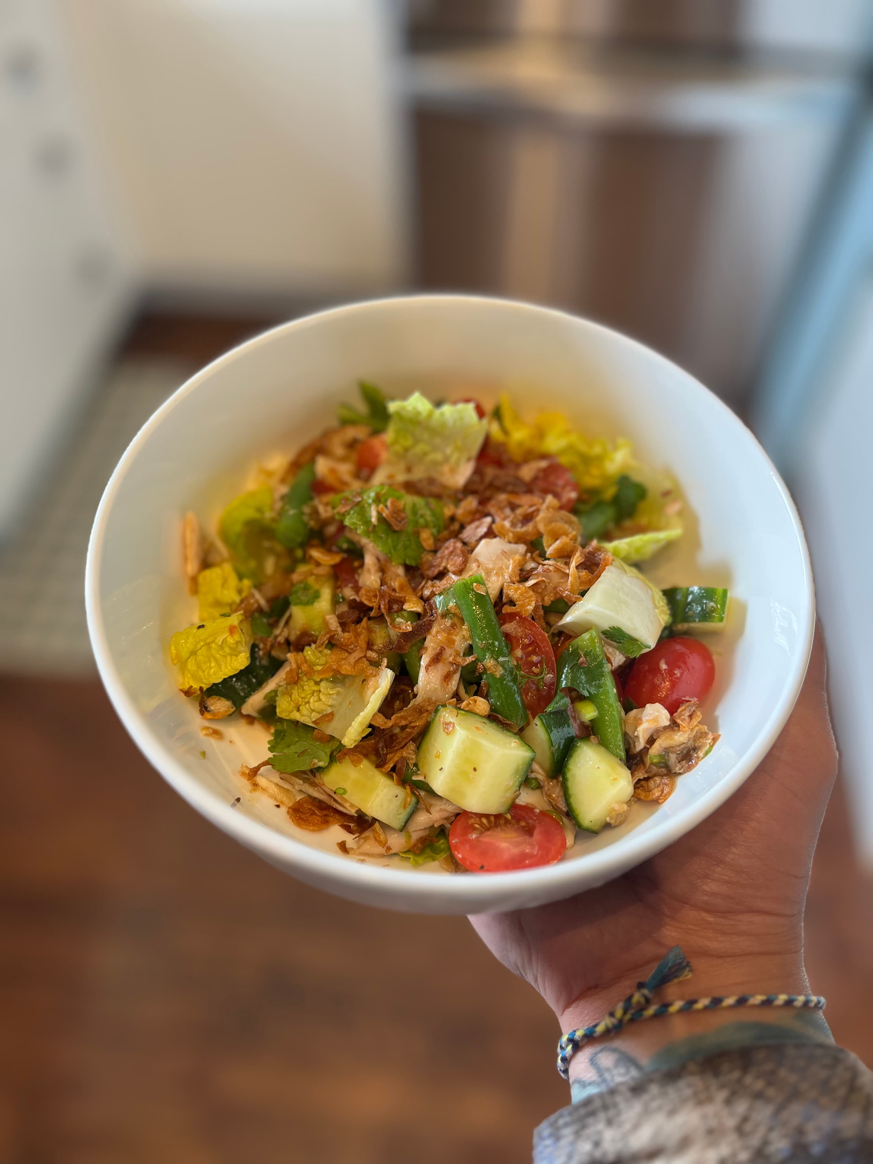 Thai chicken salad in a bowl, topped with chicken, green beans, tomaatoes, herbs, and an addictive thai dressing.
