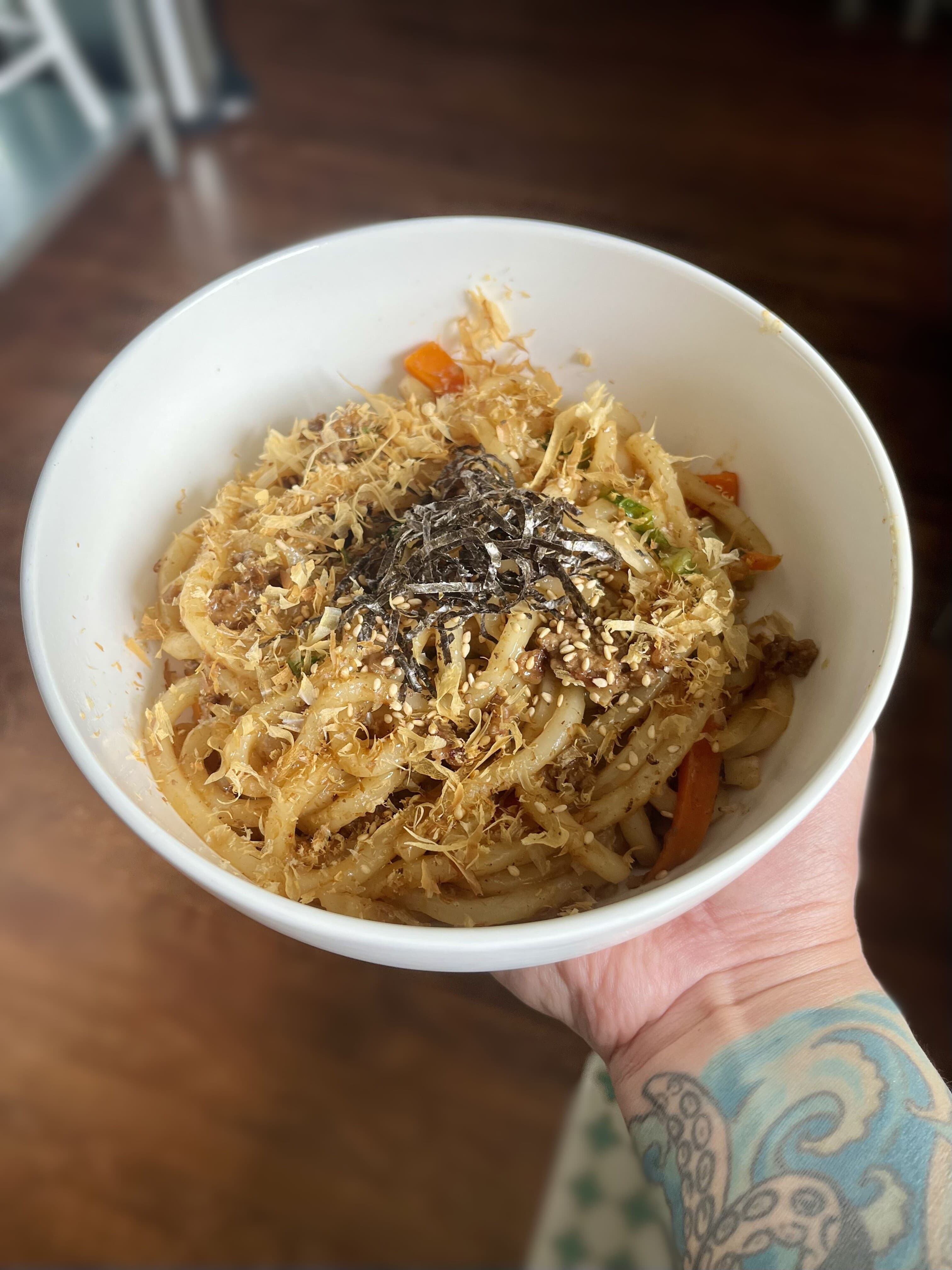 Yaki Udon in a bowl, topped with veggies and protien of choise, and an umami forward sauce.